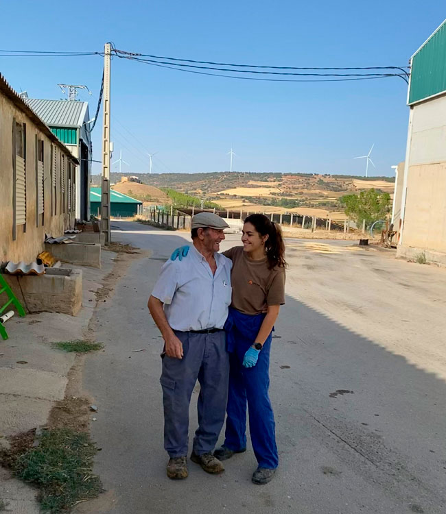 Veterinaria de campo conversando con un ganadero en el exterior de una granja porcina, en un entorno rural y soleado